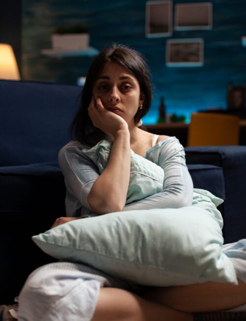 Portrait of sad person with depression problems in living room, sitting on floor and having suicidal thoughts. Depressed anxious woman in pain having mental health difficulties.